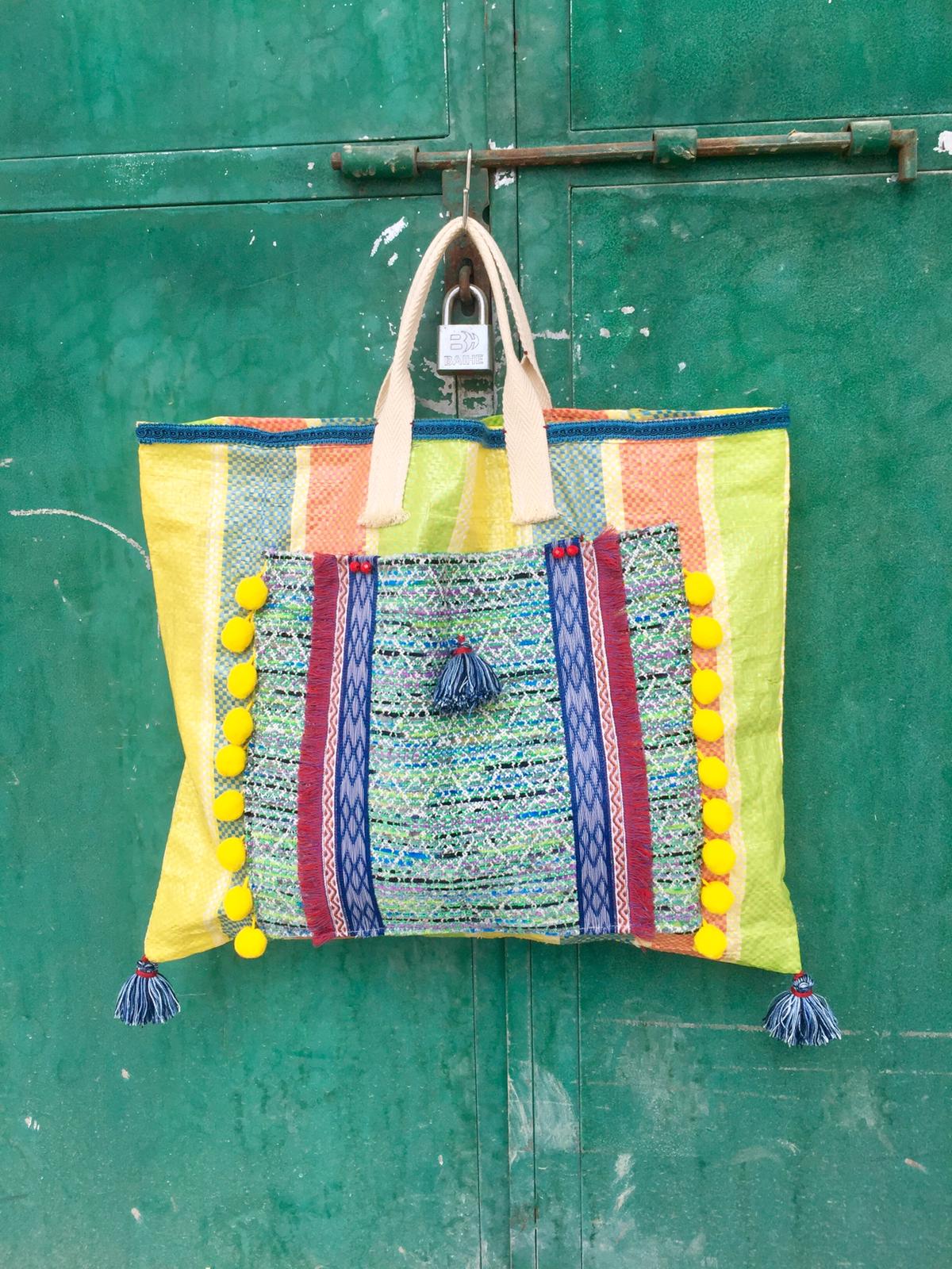 Bolso de plástico reciclado decorado con telas, pasamanerías y borlones de diferentes colores