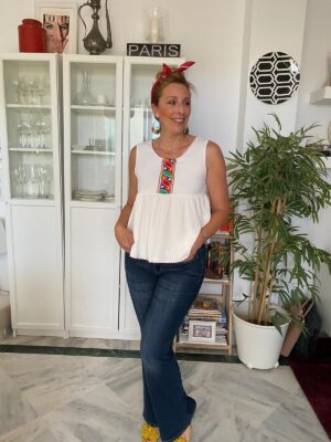 top blanco con tirantes con corte bajo el pecho y ribete bordado en colores muy vivos con jeans acampanados