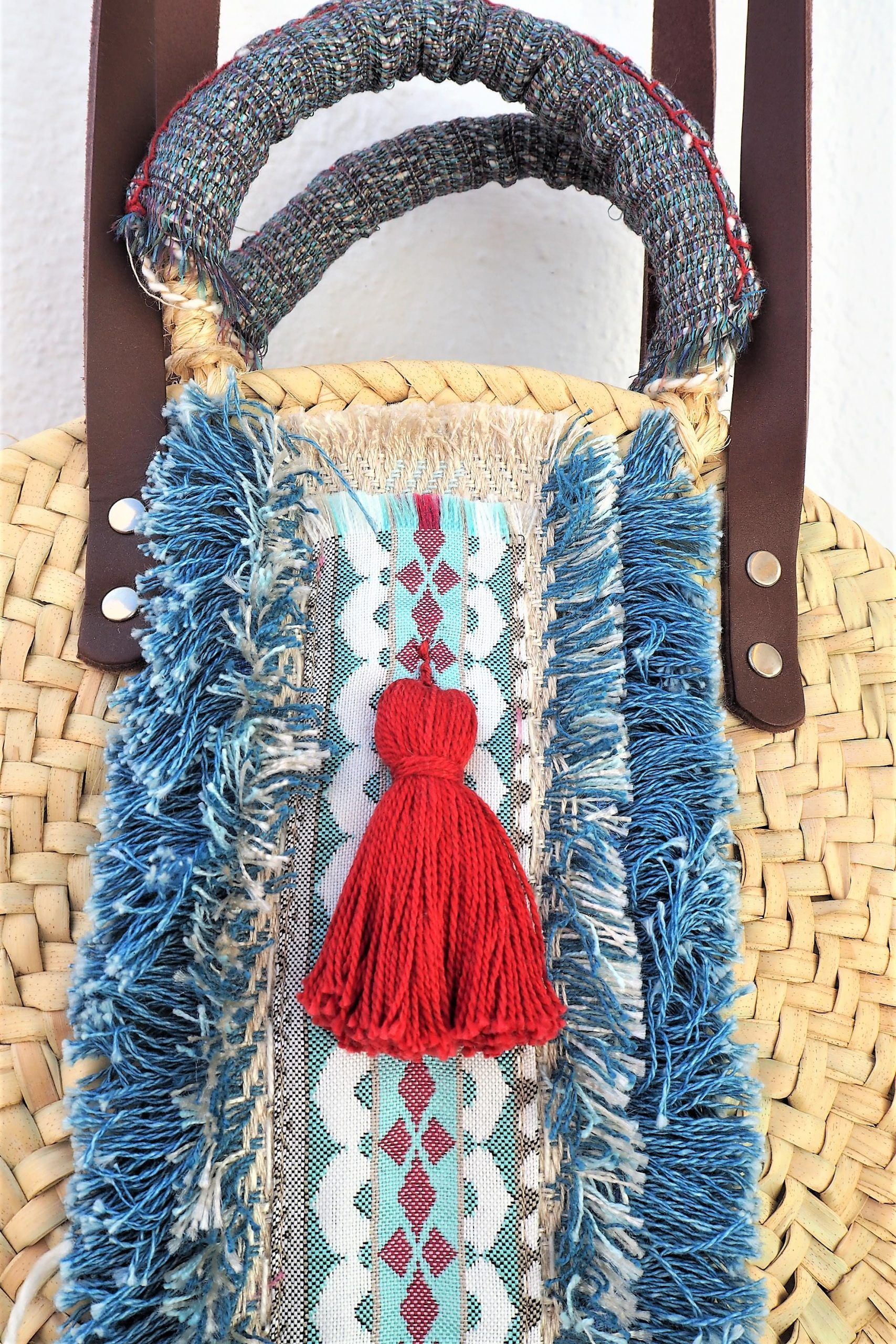 bolso capazo de palma decorado con bordados y borlones en tonos azules y rojos